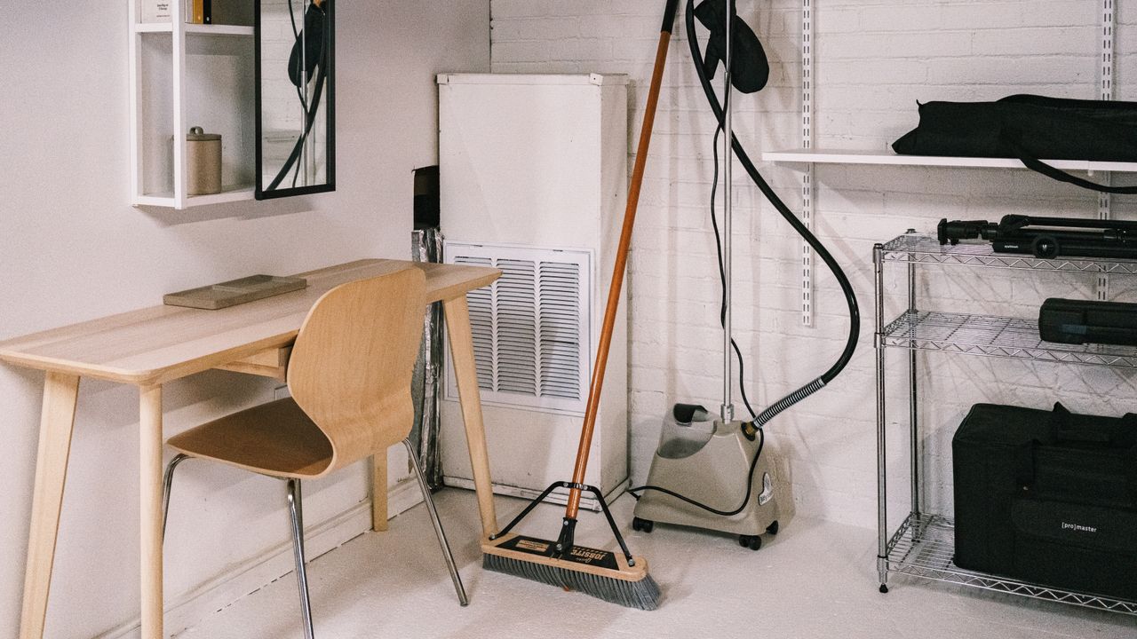 A neat home office setup with a wooden desk and chair, plus a broom and cleaning tools.